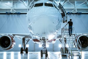 An airplane in a hangar. On a staircase to the aircraft entrance stands a man.